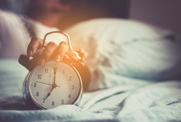 Frau mit Einschlafproblemen stellt den Wecker morgens ab