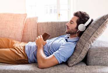 Mann schläft auf Sofa ein, während er Musik hört mit Kopfhörern