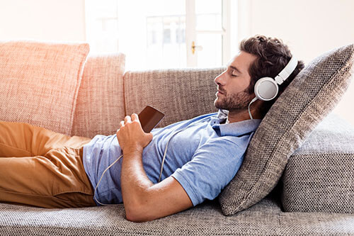 Mann schläft auf Sofa ein, während er Musik hört mit Kopfhörern