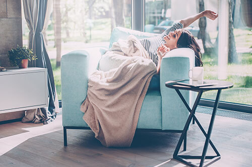 Frau streckt sich freudestrahlend und ausgeschlafen in Sessel im lichtdurchflutetem Wohnzimmer