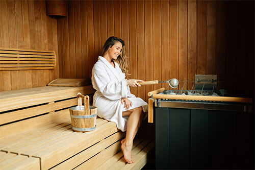 Frau sitzt mit Bademantel in Sauna und macht einen Aufguss, um in der Sauna abzunehmen