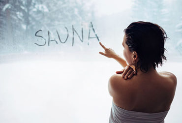 Eine Frau schreibt das Wort "Sauna" auf eine beschlagene Fensterscheibe