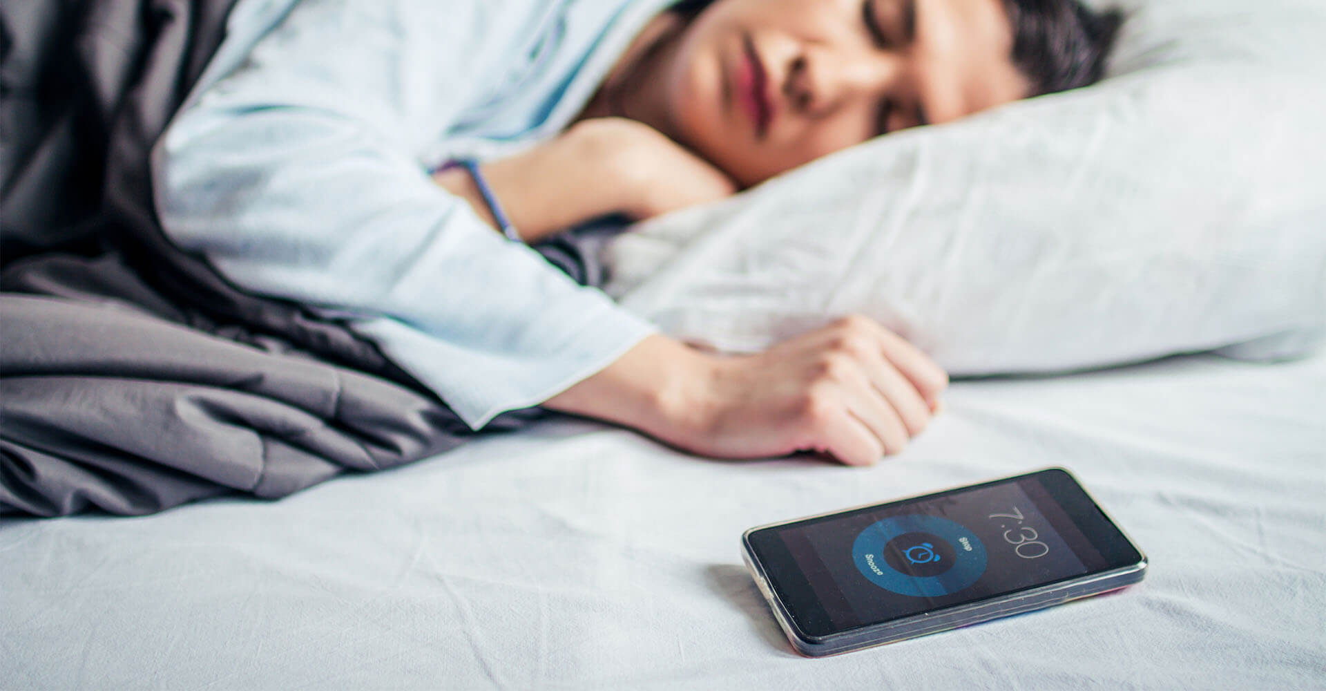 Frau schläft im Bett mit Schlafphasenwecker und per Bluetooth verbundenen Smartphone