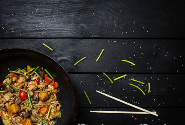 Wok auf schwarzem Holz neben Erbsenschoten und Stäbchen
