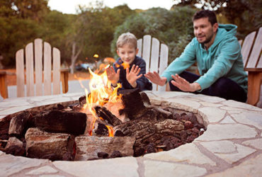 Vater und Sohn wärmen sich an Feuerstelle im Garten