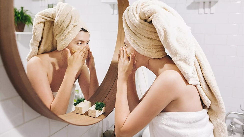 Frau mit Gesichtsmaske vor dem Spiegel im Bad
