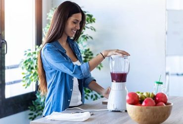 Frau bedient Smoothie Mixer in Küche
