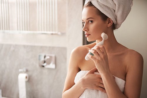 Frau mit Gesichtsreinigungsbürste in Bad