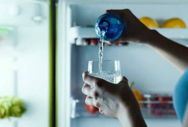 Frau trinkt Wasser aus Wassersprudler mit Glasflasche