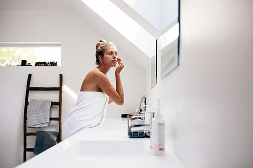 Frau trägt Feuchtigkeitscreme in Badezimmer auf
