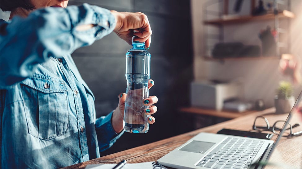 Frau öffnet Wasser-Glasflasche bei Arbeit zuhause
