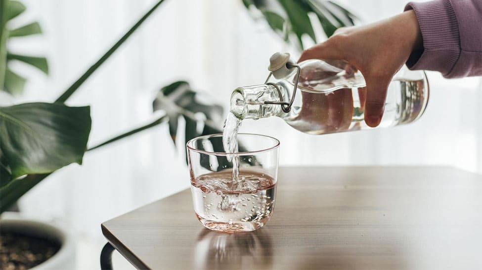 Wasser aus Wassersprudler mit Glasflasche in Glas