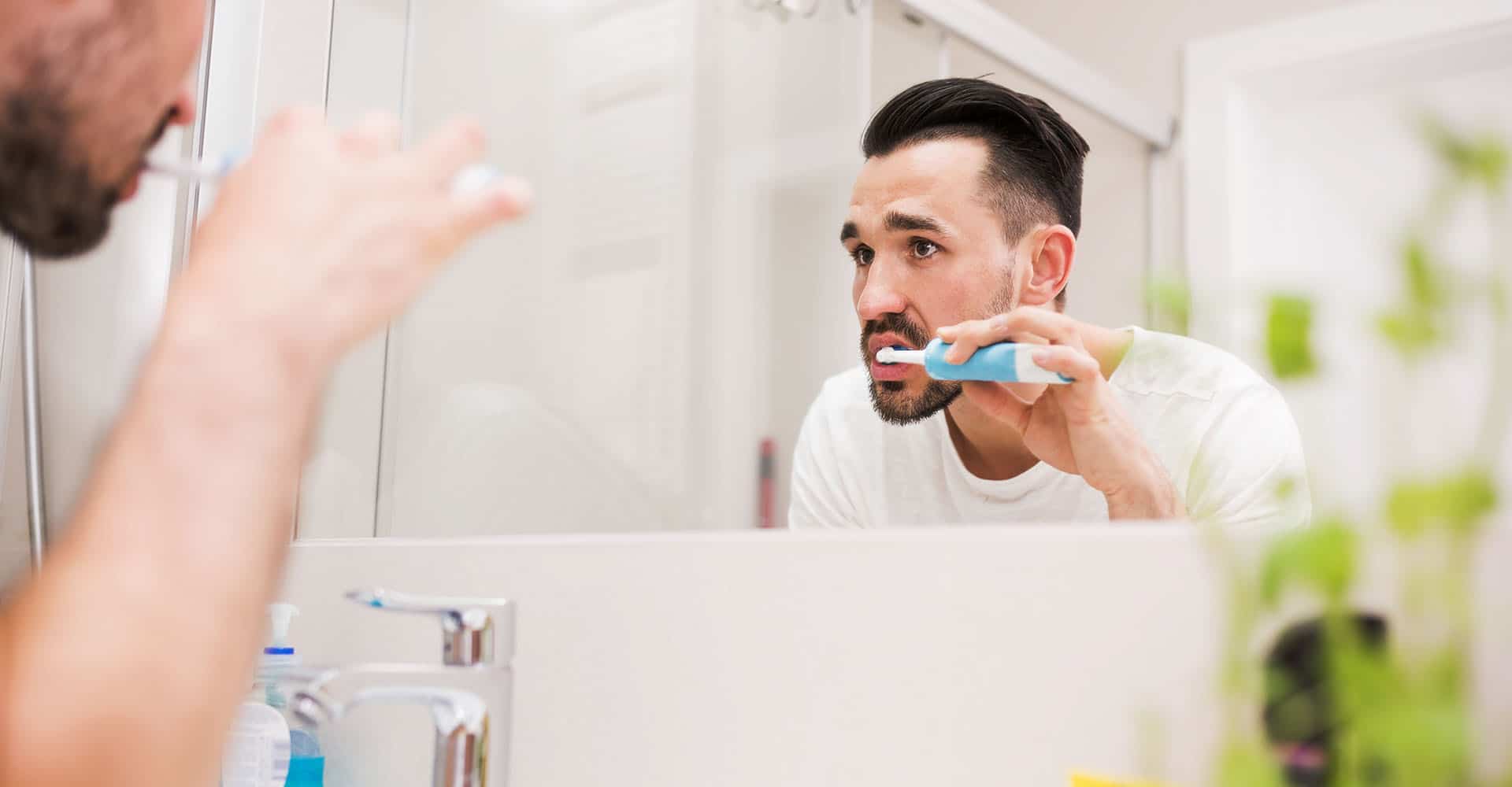 Mann putzt sich Zähne mit elektrischer Schallzahnbürste
