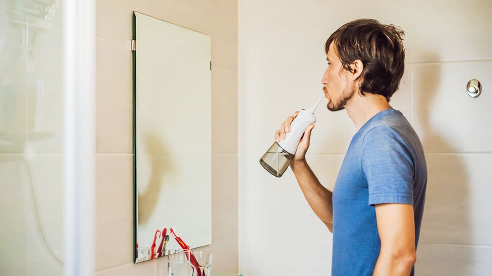 Mann verwendet Munddusche in Badezimmer