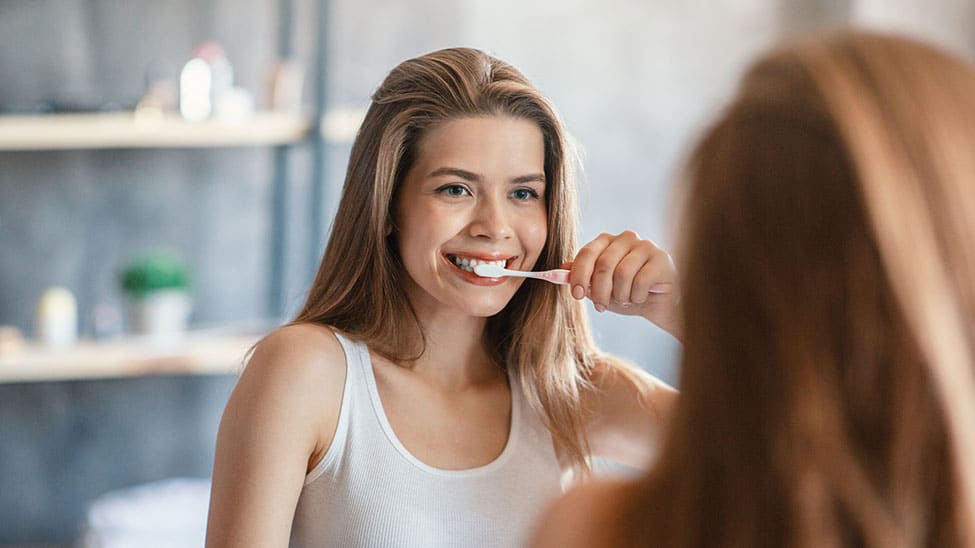Frau schaut beim Zähneputzen in Spiegel