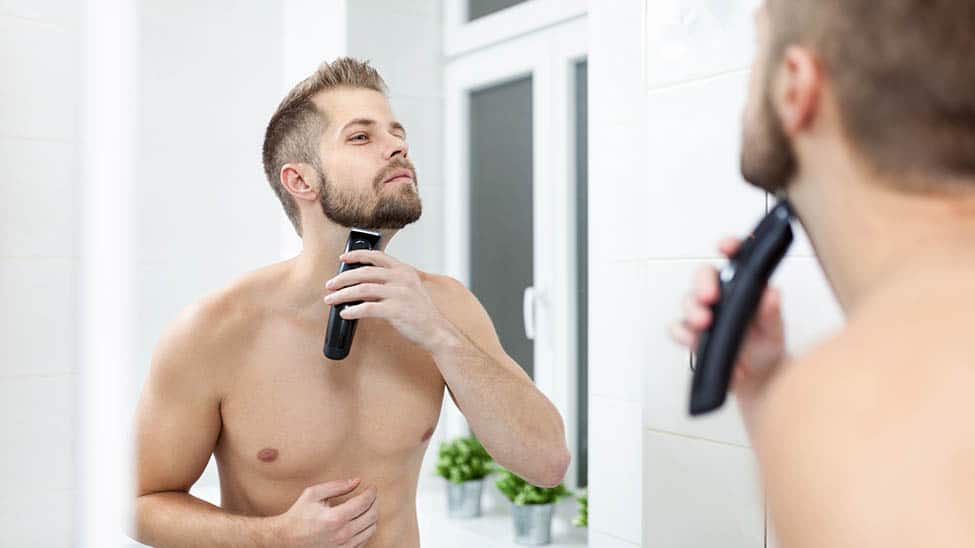 Mann rasiert sich mit Rasierapparat vor Spiegel