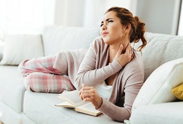 Frau auf Sofa mit Nackenschmerzen