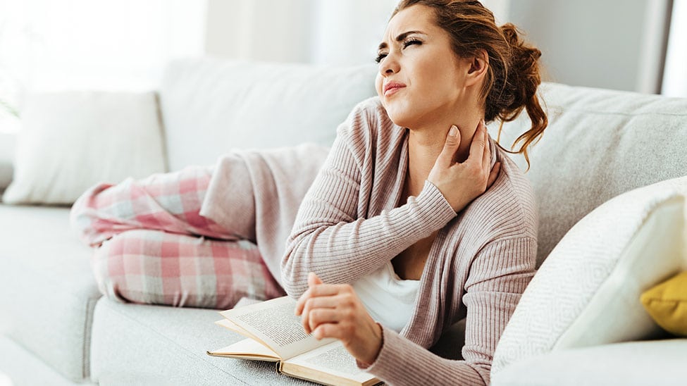 Frau auf Sofa mit Nackenschmerzen