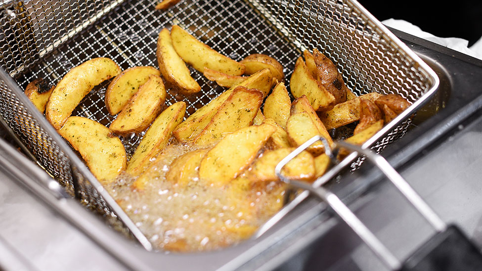 Kartoffeln in Fritteuse mit kochendem Fett