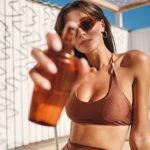 Frau in Bikini sprüht Sonnencreme für Gesicht