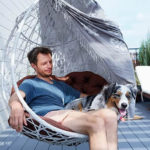 Mann sitzt mit Hund in Outdoor Hängesessel