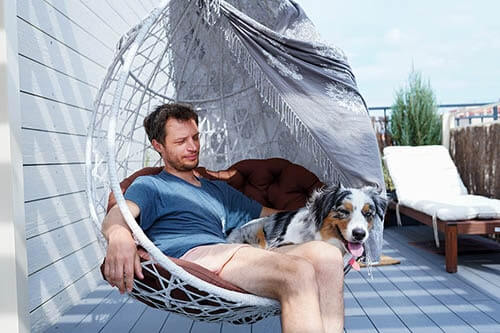 Mann sitzt mit Hund in Outdoor Hängesessel